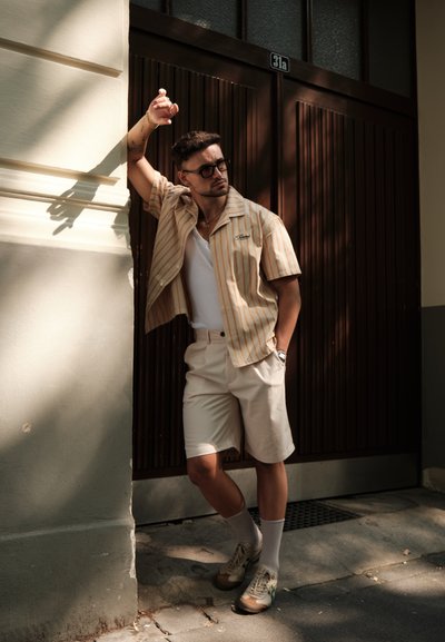 Camisa de manga corta a rayas en beige con blanco, combinada con pantalones cortos de color claro, camiseta blanca y zapatillas, complementada con gafas.