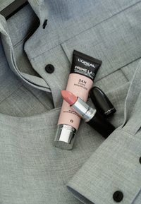 Grå tygskjorta med en svart knapp, L'Oréal Prime Lab rosa tub och MAC läppstift i ett silver- och svart hölje, som visar en mjuk rosa färg.