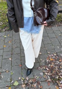 Pantaloni ampi in velluto a coste color crema abbinati a una maglietta azzurro chiaro con pizzo sotto una giacca di pelle marrone scuro; scarpe nere e borsa marrone.