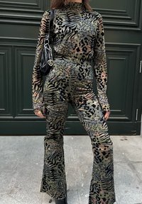 Γυναίκα που φοράει ένα γούνινο τοπ με μακριά μανίκια και καμπάνα παντελόνια με σχέδιο ζώου, κρατώντας μια μαύρη τσάντα χειρός με μπρελόκ σε σχήμα καρδιάς.