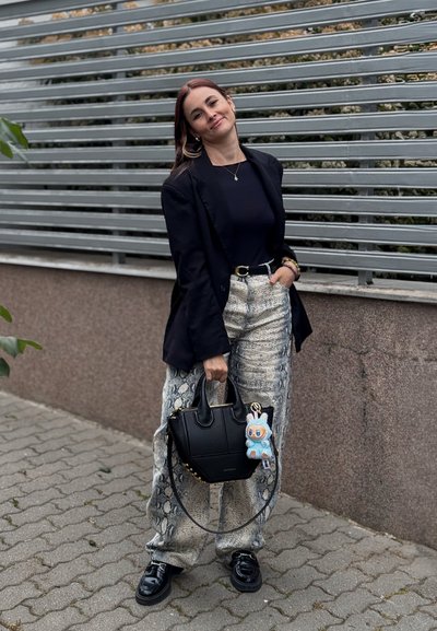 Blazer negro ajustado sobre una camiseta azul marino, combinado con pantalones de pierna ancha claros y estampados. Lleva un bolso negro con un llavero azul de acento.