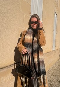 Pruun seemisnahkan mantel, beeži ja pruuni mustriga sall, must käekott ja tumedad päikeseprillid. Tumeda pluusi peal päikeselises õues.