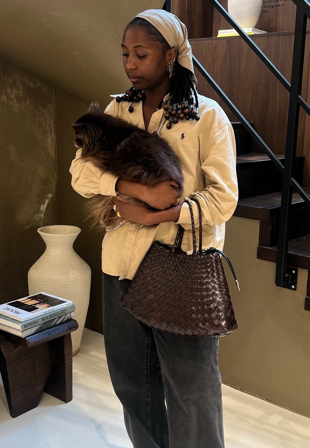 Vevd, mørkebrunt skinntote med en strukturert form og to flettede håndtak. Beige skjorte med krage, holder en fluffy brun hund.