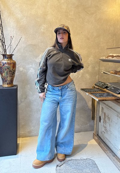 Sudadera corta de cremallera gris oscuro con rayas blancas, jeans de pierna ancha azul claro y botas de plataforma beige, en un fondo de pared texturizada.
