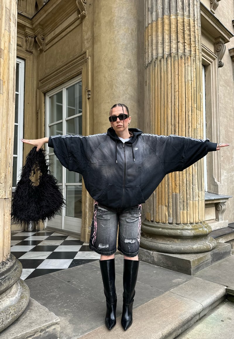 Felpa nera oversize con cappuccio e maniche larghe, shorts in denim grigio consumato, stivali neri alti sopra il ginocchio con tacco e borsa nera morbida e pelosa.