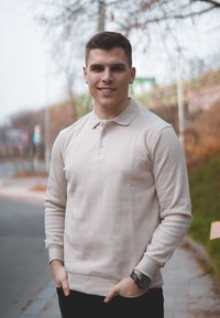 Μπεζ μακρυμάνικo πόλο πουκάμισο με σχέδιο γιακά, που διαθέτει τριπλό κουμπί. Φορεμένο με μαύρο παντελόνι και ασημένιο ρολόι.