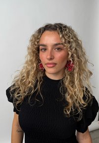 Svart, teksturert topp med puffermer; modellen har langt, krøllete blondt hår og røde blomsterøredobber; nøytral bakgrunn.