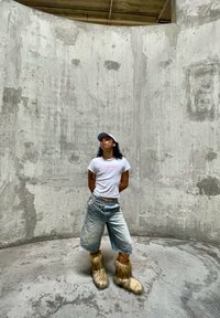 Vit T-shirt med rosa text, ljusblå denimshorts och pälsstövlar i beige och brunt. Betongbakgrund med minimal struktur.