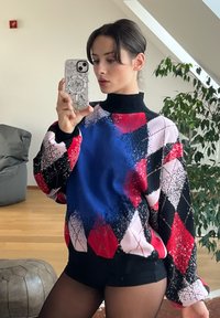 Χρωματισμένο φαρδύ πουλόβερ με διαμαντέ σχέδιο σε μπλε, ροζ, μαύρες και κόκκινες περιοχές. Υψηλή λαιμόκοψη, μακριά μανίκια και μαλακή υφή.