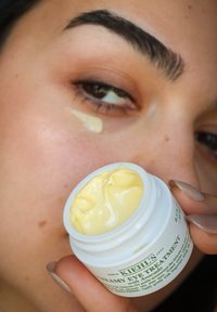 Kiehl's Romige Oogbehandeling met Avocado in een witte pot, heeft een dikke gele crèmetextuur en groene tekst op het etiket.