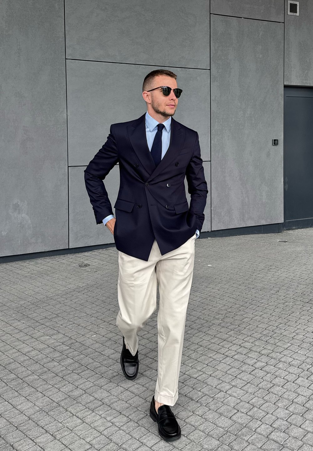 Mornarica dvoredna sakoa, svijetloplava košulja, tamna kravata, bež hlače, crne cipele; elegantan dizajn s modernim završetkom.