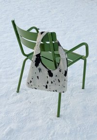Chaise en métal verte sur la neige avec un sac d'épaule noir et blanc à taches suspendu à son dossier.