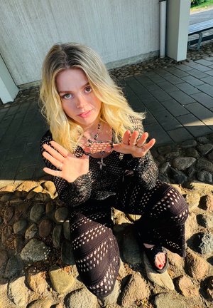 Conjunto de punto negro con un patrón de malla abierta, que incluye mangas largas y pantalones acampanados. Los accesorios notables incluyen collares en capas y anillos.