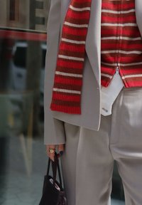 Lichtgrijze op maat gemaakte pak met ontspannen broek en een zipjack, gecombineerd met een rood gestreept gebreid sweater en een donkere handtas.