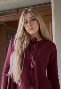Cardigan burgund tricotat, cu design cu funda în față, mâneci lungi și textură moale, completat de ochelari rotunzi.