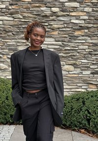 Zwarte oversized blazer over een zwart geribbelde crop top, gecombineerd met zwarte losvallende broek. Zilveren oorbellen in de vorm van een ring en een hartjeshanger ketting.