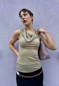 Ανοιχτό μπεζ αμάνικο τοπ με λαιμόκοψη cowl, συνδυασμένο με μια μαύρη φούστα και μια μωβ τσάντα. Η ασημένια κοσμηματολογία ενισχύει την εμφάνιση.