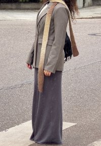 Brun rutete blazer med tekstur, grå lang skjørt og et strikket skjerf med brune gradienttoner; et tilbehør inkluderer en svart frynsete veske.