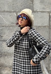 Black and white checkered dress with long sleeves, cream wool beret, oversized blue sunglasses, and a black handbag with a lace detail.