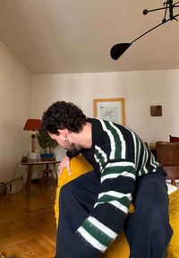 Canapé jaune rembourré aux bords arrondis et à la capitonnage vertical, accompagné d'une personne portant un pull rayé noir et blanc, dans un cadre de salon.