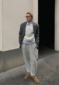 Grå oversized blazer over en lys genser, med en blå skjorte med krage og grå joggebukser. Beige slip-on sko. Glatte teksturer, avslappet passform.