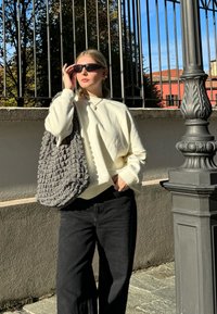 Weißes oversized Sweatshirt, schwarze weite Hose und eine strukturierte graue Tasche. Die Accessoires umfassen elegante schwarze Sonnenbrille und eine silberne Halskette.