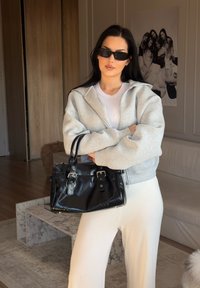 Sweatshirt cinza com fecho, top branco, calças creme e mala preta. Tecido suave, forma estruturada e acessórios em prata na mala.