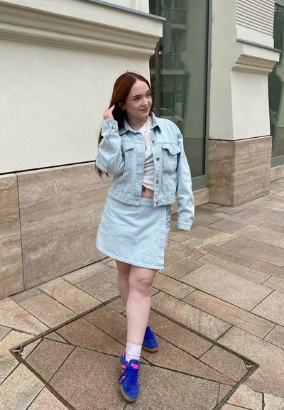 Chaqueta de mezclilla azul claro y falda a juego, combinadas con zapatillas de deporte azules y rosas. El atuendo cuenta con una parte superior corta por debajo.