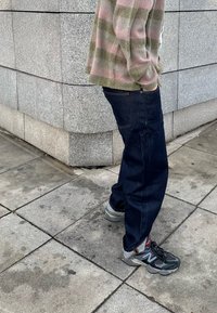 Jean en denim foncé à coupe droite, associé à des chaussures de course grises avec des accents rouges. Porté avec un pull rayé vert clair et rose.