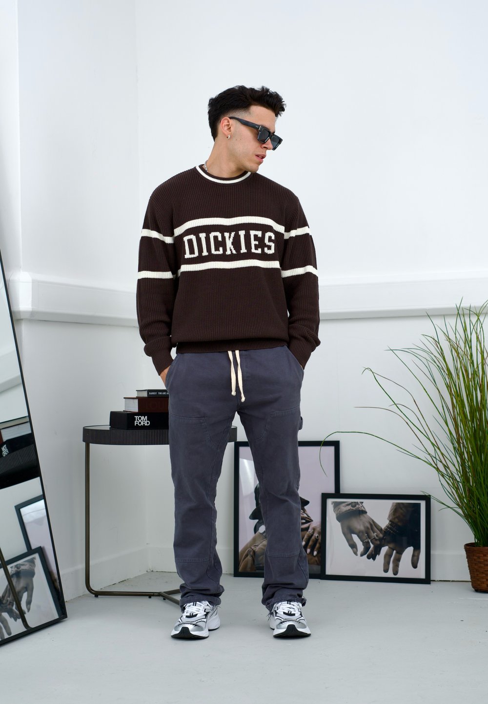 Smeđi rebrasti pulover s bijelim prugama i natpisom "DICKIES", u kombinaciji s muškim sivim cargo hlačama i bijelim tenisicama, u minimalističkom interijeru.