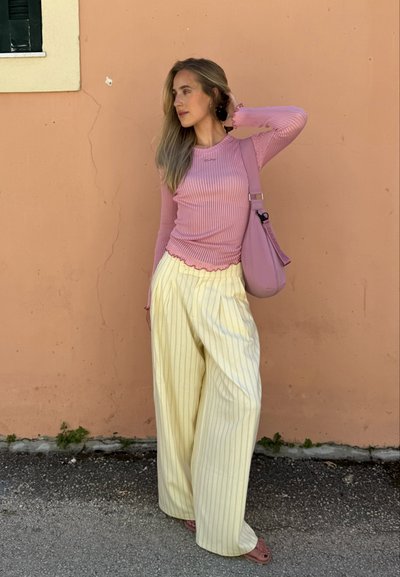 Top de manga larga de color rosa claro con borde ondulado, combinado con pantalones de pierna ancha de rayas amarillas. Lleva un bolso de hombro rosa claro.