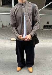 Brūnas un krēmkrāsas svītrains pogām aiztaisāms krekls, valkāts pār baltu T-kreklu; kombinēts ar melnām vaļīgām biksēm un brūnām zābakām. Pāri plecam pārnests vēstneša soma.