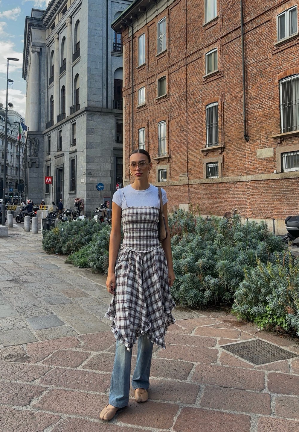 Geruite jurk met een gerimpelde zoom over lichtblauwe jeans, gecombineerd met beige flats. Eenvoudig wit T-shirt eronder, bruine schoudertas.