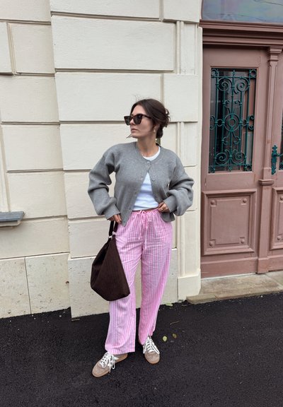 Cardigan gris de canalé, top blanco, pantalones anchos a rayas rosas, bolso tote marrón y zapatillas grises, con un fondo de pared texturizada y puerta.
