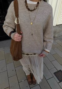 Pulover bej din lână cu mâneci lungi, purtat peste o cămașă albă. Fustă plisată crem, geantă maro din piele întoarsă și cizme maro până la gleznă. Accente de bijuterii aurii.