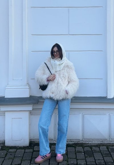 Chaqueta de piel sintética en beis claro, de corte oversized; combinada con jeans de mezclilla azul claro y zapatillas rosas. Sudadera blanca de punto debajo.