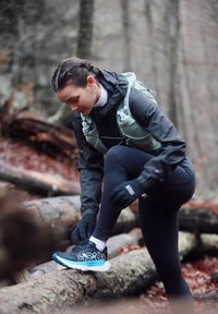 Chaussure de course noire et bleu sarcelle avec un design à lacets et une tige en mesh, associée à un legging noir ajusté et un sweat à capuche gris avec des accents réfléchissants.