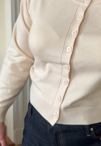 Ljusbeige kofta i mjukt stickat tyg, med rund halsringning och knäppning framtill. Standardpassform med ribbade detaljer.