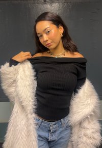 Svart ribbet av skulderen topp kombinert med lyseblå denimjeans og en fluffy hvit pelsjakke. Gullkjede med hjerteapplikasjoner.