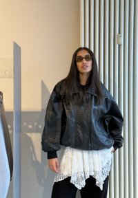 Fekete bőr, túlméretezett dzseki magas gallérral, fehér csipkés tunika fölött rétegezve. Fekete nadrág és sötét napszemüveg teszi teljessé a megjelenést.