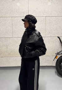 Mustast nahast lühike jakk kõrge kraega, kantud musta kaelusega üle. Sobitatud mustade dressipükstega, mille külgedel on valged triibud.