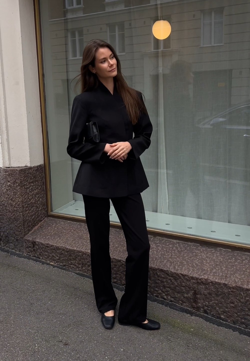 Veste noire sur mesure avec un col haut, assortie à un pantalon noir à jambe large. Design épuré, détails minimaux et texture de tissu lisse.