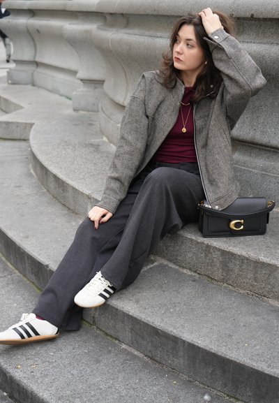 Chaqueta gris de espiga, top burdeos, pantalones negros de cintura alta, zapatos blancos con rayas negras y bolso negro con detalles dorados.