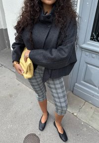 Harmaa villatakki korkealla kauluksella, harmaamusta ruutukuosiset lyhytlahkeiset housut, mustat ballerinat ja keltainen clutch-laukku.