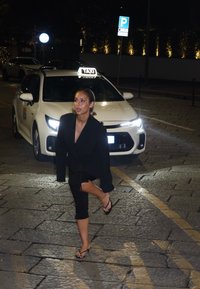 Svart oversized blazer, svarte leggings og flip-flops. Kveldsinnstilling med en hvit taxi i bakgrunnen, opplyste gateskilt. Steinbelagt fortau.