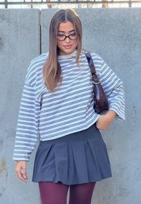 Cămașă cropată cu mâneci lungi, în dungi albe și bleumarin; asociată cu o fustă plisată bleumarin și ciorapi burgundy; geantă maro lucioasă ca accesoriu.