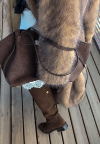 Barna hasított bőr kézitáska sima felülettel, vékony fogantyúval. Párosítva barna térd fölé érő csizmával és csíkos mintás műszőrme kabáttal.