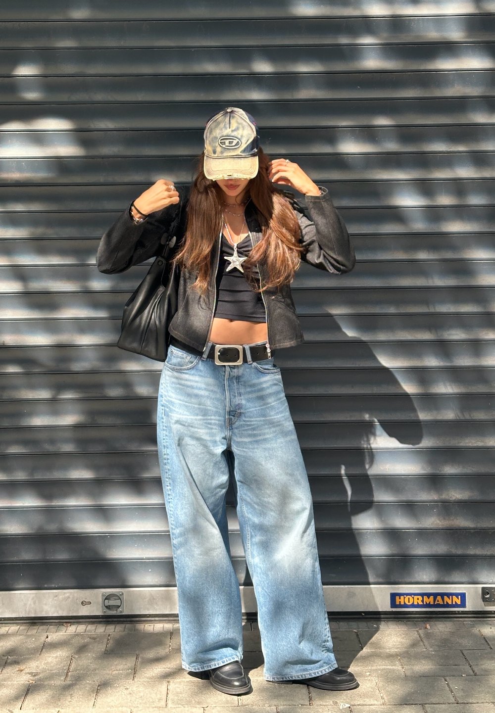 Čierna kožená bunda, skrátený čierny top, široké svetlo modré rifle, čierna šiltovka v cargo štýle, čierna kabelka, strieborný náhrdelník so zákonom.