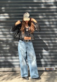 Čierna kožená bunda, skrátený čierny top, široké svetlo modré rifle, čierna šiltovka v cargo štýle, čierna kabelka, strieborný náhrdelník so zákonom.