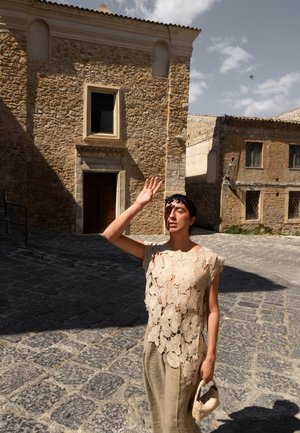 Top de croché suelto, beige, con patrones florales, superpuesto a una falda de lino clara. Tonos naturales, detalles texturizados y un bolso de mimbre complementan el conjunto.